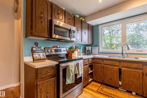 Kitchen featuring wood-finish cabinetry, light countertops, and a double-basin stainless steel sink - 33 Andrew Crescent, St. Albert, AB 