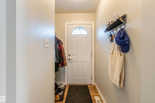 Entryway featuring a white paneled door with an arched glass insert, light wood-finish flooring, and a wall-mounted organizational rack - 33 Andrew Crescent, St. Albert, AB 