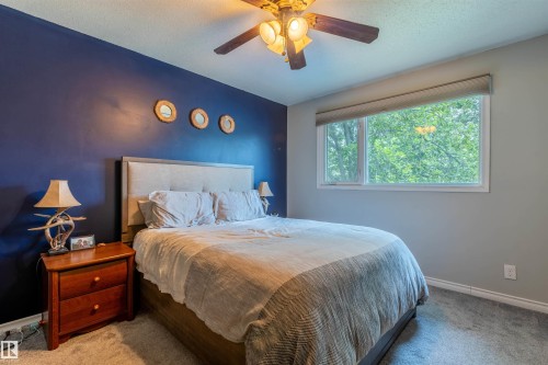 Bedroom featuring a ceiling fan with integrated lighting, a large window, and carpet flooring - 33 Andrew Crescent, St. Albert, AB 
