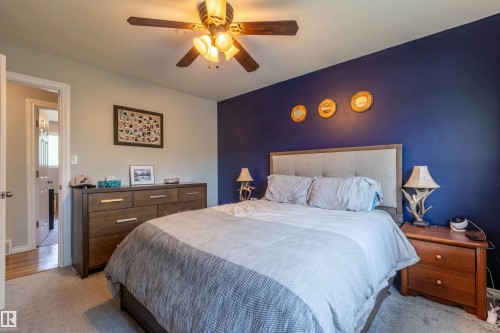 Carpeted bedroom featuring a ceiling fan with integrated lighting, a contrasting accent wall, and a framed bed with an upholstered headboard - 33 Andrew Crescent, St. Albert, AB 