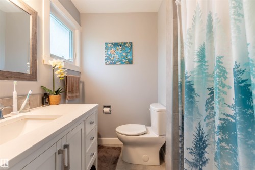 Bathroom featuring a single vanity with an integrated sink, a rectangular mirror with a wood-finish frame, a window, and a toilet - 33 Andrew Crescent, St. Albert, AB 