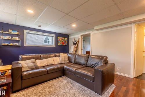 Recreation room featuring hardwood-style flooring, a drop ceiling with recessed lighting, a window with blinds, and white trim - 33 Andrew Crescent, St. Albert, AB 