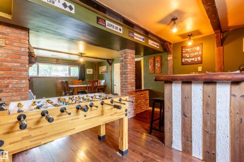 Lower-level recreation space featuring brick columns, wood-finish flooring, a built-in bar with a wooden countertop and paneled base, and exposed ceiling beams - 33 Andrew Crescent, St. Albert, AB 