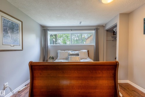Bedroom featuring wood-finish flooring, a rear window with drapes, and an open closet space - 33 Andrew Crescent, St. Albert, AB 