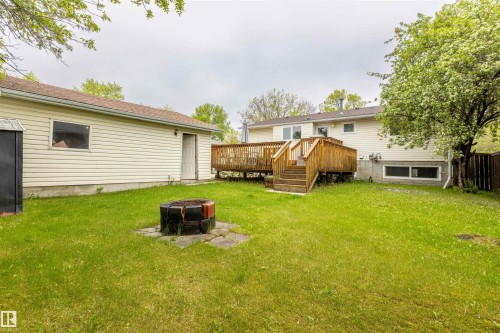 Expansive backyard with a wooden deck and stairs, featuring a freestanding fire pit on a stone paver base - 33 Andrew Crescent, St. Albert, AB 