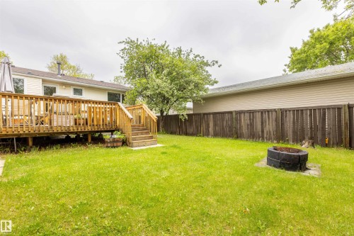 Expansive green lawn featuring a wood deck, wood privacy fence, and a stone fire pit - 33 Andrew Crescent, St. Albert, AB 