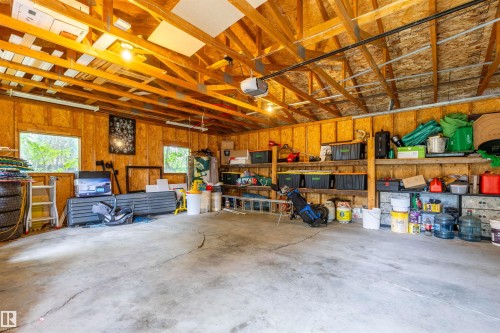 Spacious garage featuring exposed wood beam ceiling, concrete flooring, two windows, wall-mounted shelving, and an automatic garage door opener - 33 Andrew Crescent, St. Albert, AB 