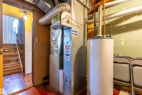 Utility area featuring a water heater and furnace with exposed ductwork, concrete walls, and a wood-finish staircase with a handrail - 33 Andrew Crescent, St. Albert, AB 