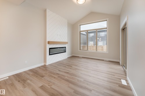 Contemporary living room featuring wood-finish flooring, a vaulted ceiling, and a fireplace with a chevron-patterned surround and a wood mantel - 115 Garneau Gate, Spruce Grove, AB 