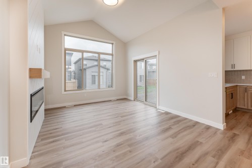 Spacious living area featuring vaulted ceilings, wood-finish flooring, and a contemporary fireplace with a wood mantle - 115 Garneau Gate, Spruce Grove, AB 