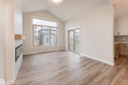 Spacious living area featuring vaulted ceilings, wood-finish flooring, and a contemporary fireplace with a wood mantle - 