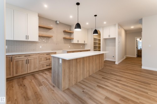 Modern kitchen featuring a large central island with a white countertop, two pendant lights, and wood-finish cabinetry - 115 Garneau Gate, Spruce Grove, AB 