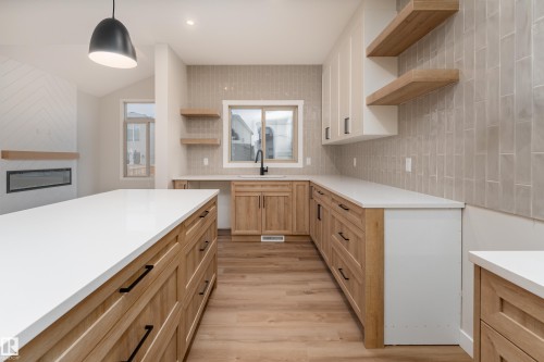 Open-concept kitchen featuring a large island with white countertops, light wood-finish cabinetry with black hardware, and wood-finish flooring - 115 Garneau Gate, Spruce Grove, AB 