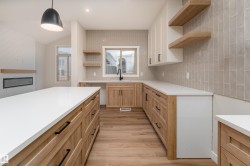 Open-concept kitchen featuring a large island with white countertops, light wood-finish cabinetry with black hardware, and wood-finish flooring - 