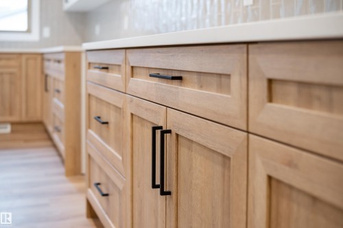 Light wood cabinetry with matte black hardware, solid surface countertops, and a tiled backsplash - 115 Garneau Gate, Spruce Grove, AB 