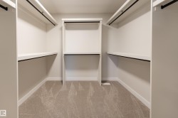 Walk-in closet featuring white built-in shelving, multiple hanging rods, and light-toned carpeting - 