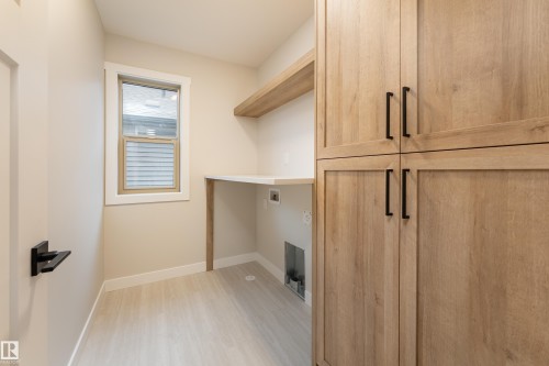 Utility room featuring wood-finish cabinetry with matte black hardware, built-in shelving, a workstation countertop, and light wood-finish flooring - 115 Garneau Gate, Spruce Grove, AB 