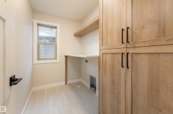 Utility room featuring wood-finish cabinetry with matte black hardware, built-in shelving, a workstation countertop, and light wood-finish flooring - 