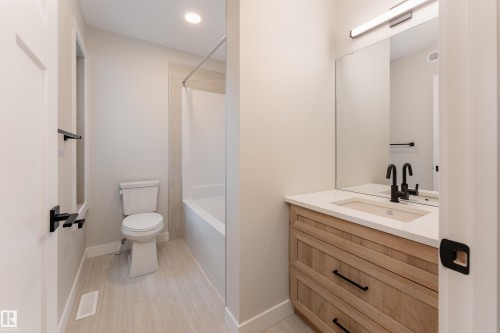 Bathroom featuring a light wood-finish vanity with a white countertop and undermount sink, black matte faucet, and large wall-mounted mirror - 115 Garneau Gate, Spruce Grove, AB 