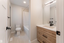 Bathroom featuring a light wood-finish vanity with a white countertop and undermount sink, black matte faucet, and large wall-mounted mirror - 