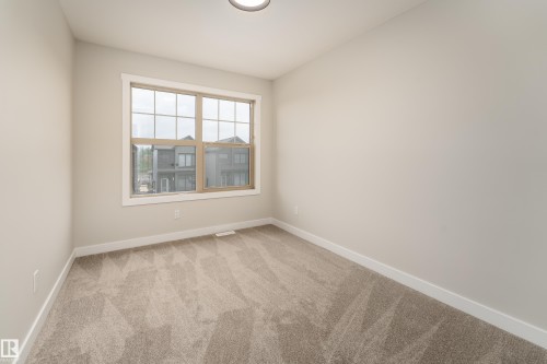 Neutral-toned room featuring a large window with white trim, light beige walls, and patterned carpeting - 115 Garneau Gate, Spruce Grove, AB 
