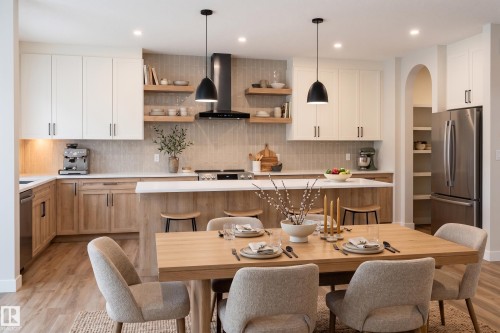 Modern kitchen featuring two-tone cabinetry, a central island with bar seating, stainless steel appliances, and wood-finish flooring - 115 Garneau Gate, Spruce Grove, AB 