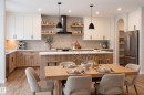 Modern kitchen featuring two-tone cabinetry, a central island with bar seating, stainless steel appliances, and wood-finish flooring - 115 Garneau Gate, Spruce Grove, AB 