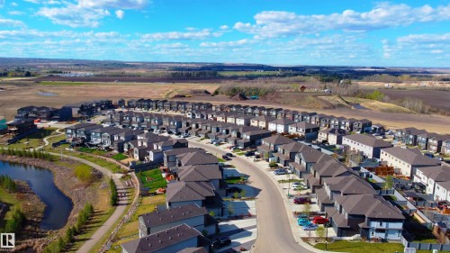 Modern residential development featuring a curved street layout, uniform architectural styles, and a stormwater pond with walking paths - 115 Garneau Gate, Spruce Grove, AB 