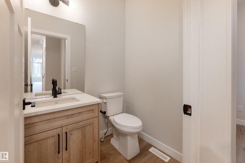 Powder room featuring a wood-finish vanity with a built-in rectangular sink, light-toned countertop, and matte black fixtures - 115 Garneau Gate, Spruce Grove, AB 