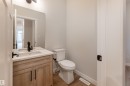 Powder room featuring a wood-finish vanity with a built-in rectangular sink, light-toned countertop, and matte black fixtures - 115 Garneau Gate, Spruce Grove, AB 