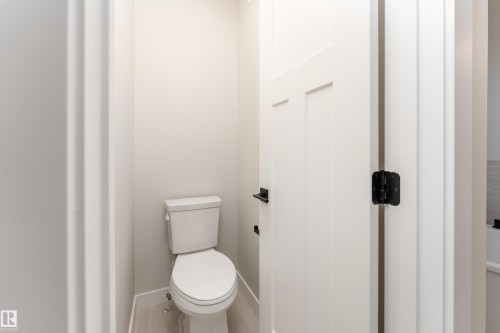 Powder room featuring a two-piece white toilet, light wood-finish flooring, and crisp white walls - 115 Garneau Gate, Spruce Grove, AB 