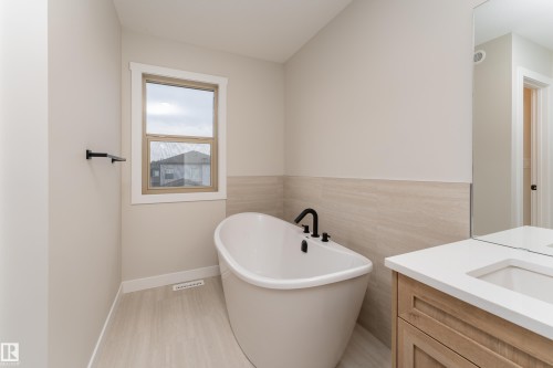 Freestanding soaking tub with matte black fixtures, complemented by light wood-finish flooring - 115 Garneau Gate, Spruce Grove, AB 