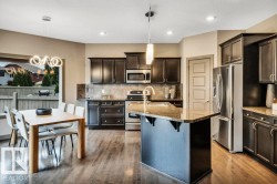 Open-concept kitchen and dining area featuring wood-finish flooring, dark wood cabinetry, a granite-top island, stainless steel appliances, and a tiled backsplash - 