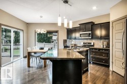 Kitchen featuring dark wood cabinetry, stainless steel appliances, a granite island with an undermount sink, and wood-finish flooring - 