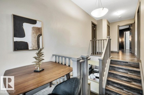 Upper-level landing featuring wood-finish flooring, a contemporary ceiling light fixture, and a staircase with a gray-painted railing and balusters - 1107 Chahley Crest, Edmonton, AB 