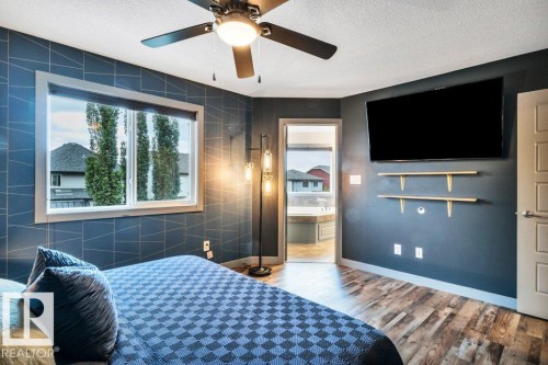 Bedroom featuring wood-finish flooring, a ceiling fan with integrated lighting, a large window, a wall-mounted television, and decorative shelving - 1107 Chahley Crest, Edmonton, AB 