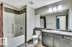 Bathroom featuring a built-in tub and shower unit, vanity with an integrated sink, dark wood-finish cabinetry, a full-width mirror, and a three-light fixture - 