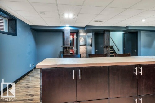 Lower level entertainment space featuring a custom island with wood-finish countertop and dark cabinetry, wood-finish flooring, and recessed lighting - 1107 Chahley Crest, Edmonton, AB 