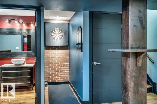 Recreation area featuring a dartboard with accent lighting, exposed brick wall, and dark wood-finish flooring - 1107 Chahley Crest, Edmonton, AB 