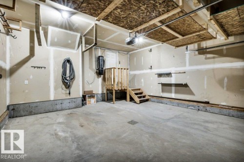 Spacious garage featuring a concrete floor, overhead storage structure, built-in shelving, and a wooden stair platform - 1107 Chahley Crest, Edmonton, AB 