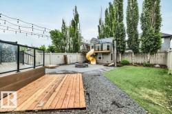 Expansive backyard featuring a new wood deck with glass railing, a stone fire pit area, a grass lawn, and a custom playhouse with a slide - 