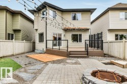 Rear exterior featuring a multi-level deck with glass panel railings, a stone-built fire pit, and string lighting - 