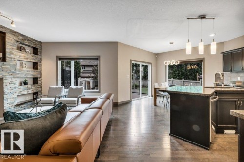 Open-concept living area featuring dark wood-finish flooring, a stacked stone accent wall with integrated shelving, and large windows - 1107 Chahley Crest, Edmonton, AB 