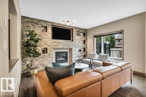 Living area featuring a stone accent wall with built-in shelving, a fireplace with an integrated television niche, dark wood-finish flooring, and a large window providing natural light - 1107 Chahley Crest, Edmonton, AB 