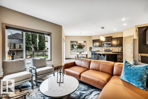 Open-concept living space featuring expansive windows, recessed lighting, wood-finish cabinetry, stainless steel appliances, and a kitchen island with seating - 1107 Chahley Crest, Edmonton, AB 