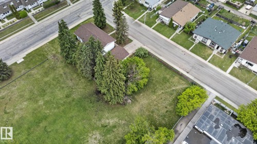 Expansive property featuring a large green space, mature evergreen trees, and a detached garage with a brown shingle roof - 13908 64 Street, Edmonton, AB 