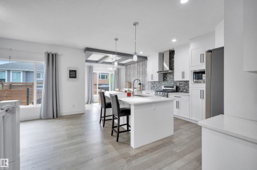 Contemporary kitchen featuring white cabinetry, stainless steel appliances, a center island with pendant lighting, and light wood-finish flooring - 3898 Robins Crescent, Edmonton, AB 