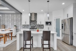 Modern kitchen featuring a central island with countertop seating, white cabinetry with contemporary hardware, stainless steel appliances, and a mosaic tile backsplash - 