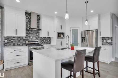 Contemporary kitchen featuring white cabinetry, stainless steel appliances, a mosaic tile backsplash, a central island with a sink, and pendant lighting - 3898 Robins Crescent, Edmonton, AB 