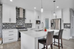Contemporary kitchen featuring white cabinetry, stainless steel appliances, a mosaic tile backsplash, a central island with a sink, and pendant lighting - 